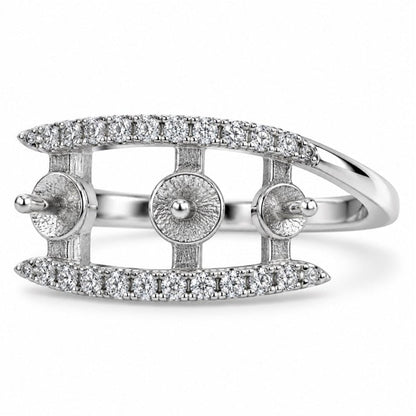 A silver-toned ring featuring a curved top and bottom band paved with small clear stones, with three circular pavé sections on the sides and a polished band, shown on a white background.